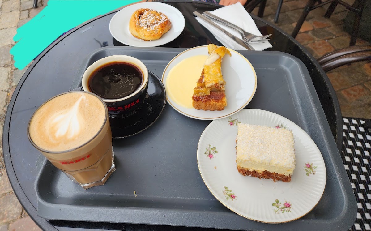 En fikabricka på uteserveringen: caffè latte, bryggkaffe, kanelbulle, äppelpaj med vaniljsås och morotskaka
